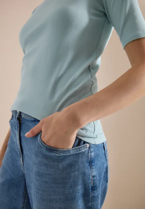 Torse d'une personne en T-shirt bleu clair, main dans la poche d'un jean bleu.