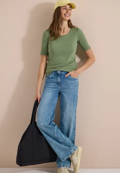 T-shirt basique à col rond en couleur unie deep matcha green Femme en t-shirt vert, jean large et baskets blanches, tenant un sac noir sur fond neutre.
