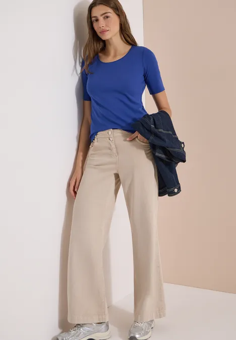 T-shirt basique à col rond en couleur unie deep river blue Femme en haut bleu moulant et pantalon beige ample, tenant une veste bleu foncé de manière décontractée.