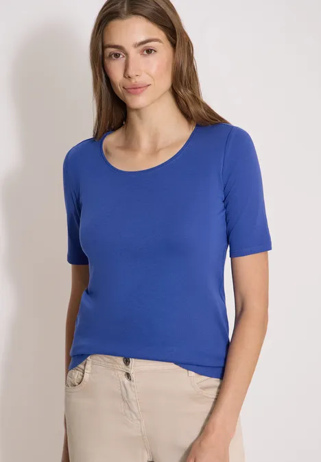 T-shirt basique à col rond en couleur unie deep river blue Jeune femme portant un t-shirt bleu à manches courtes et un pantalon beige sur fond blanc.