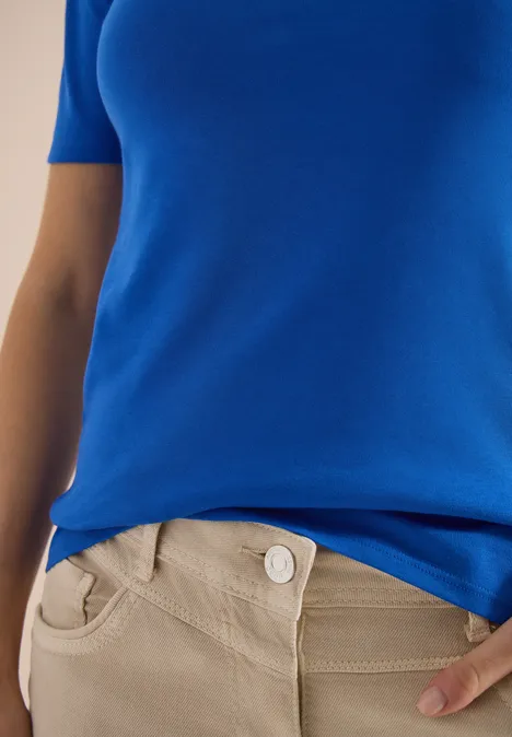 Haut bleu et pantalon beige en gros plan, cadrage du torse à la taille.