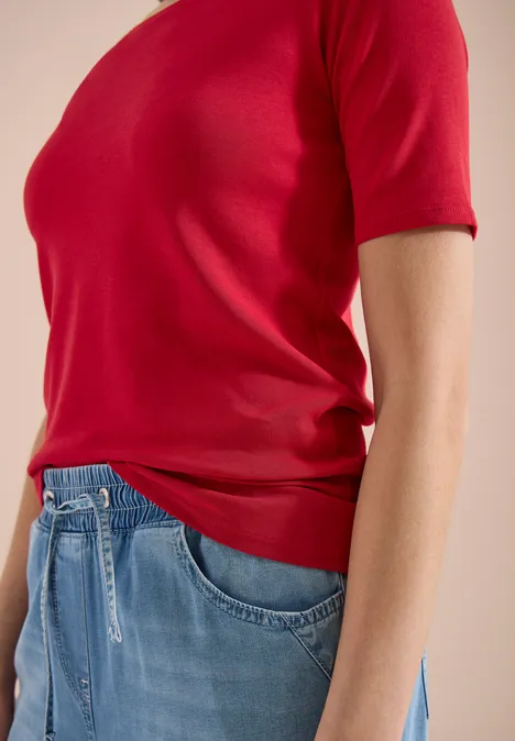 Buste d'une personne portant un T-shirt rouge à manches courtes et un jean bleu