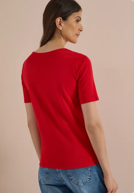 Femme vue de dos portant un t-shirt rouge et un jean bleu sur fond neutre.