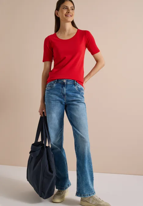 Femme avec haut rouge, jean bleu et un grand sac bleu à la main.