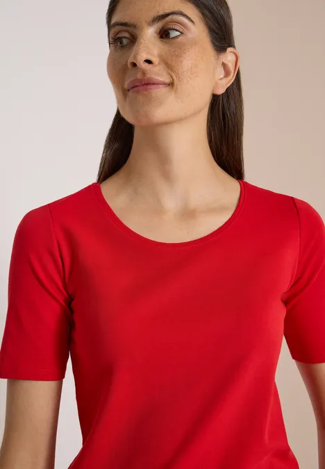 Femme portant un t-shirt rouge à manches courtes et col rond, regard légèrement de côté.