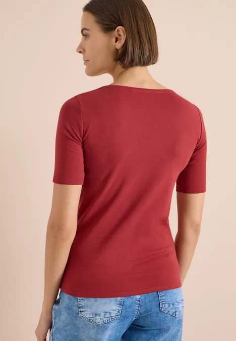 Rückenansicht einer Person in rotem Shirt mit halblangen Ärmeln und blauer Jeans.