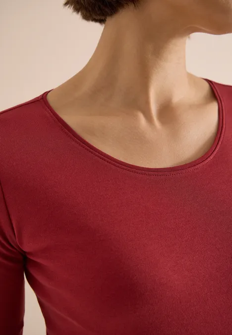 Frau trägt rotes Rundhals-Shirt, Fokus auf Hals und Schlüsselbein.