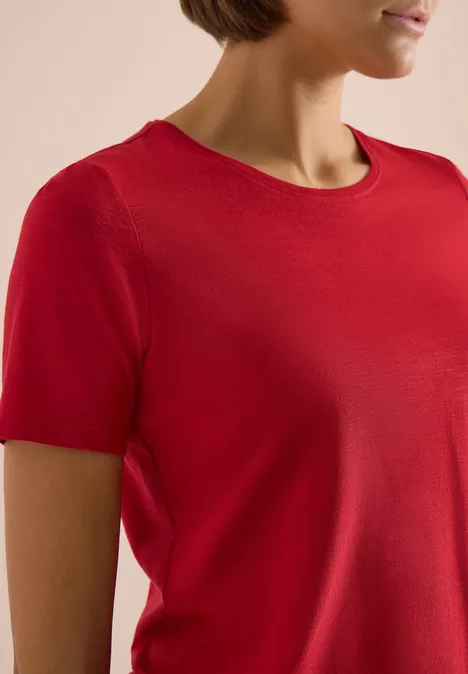 Nahaufnahme eines weiblichen Oberkörpers in rotem, kurzärmeligen T-Shirt.