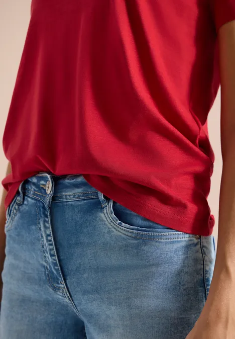 Eine Person trägt rotes T-Shirt und blaue Jeans.