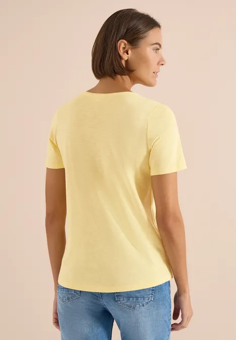 Een persoon gezien van achteren draagt een geel T-shirt en een blauwe spijkerbroek.