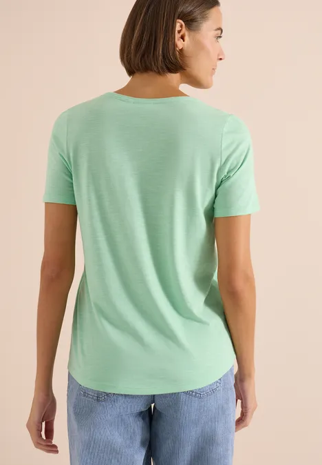 Persoon van achteren in mintgroen T-shirt en blauwe spijkerbroek tegen lichte achtergrond