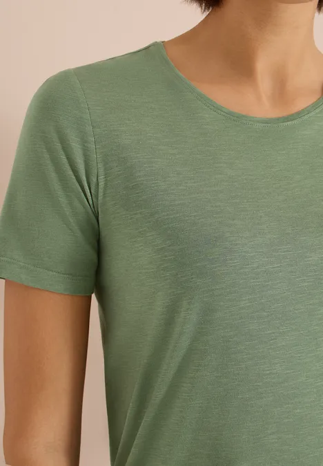 Eine Person trägt ein schlichtes, hellgrünes T-Shirt mit kurzen Ärmeln.