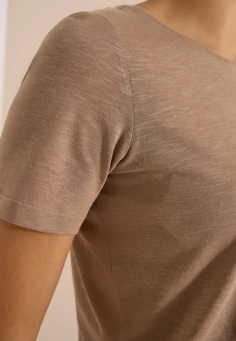 Basic Shirt met ronde hals creamy mocha Close-up van een persoon in een beige/bruin, nauwsluitend T-shirt met korte mouwen van dunne stof.