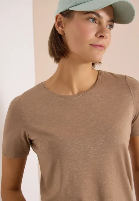 Basic Shirt met ronde hals creamy mocha Vrouw met beige T-shirt en lichtgroene pet tegen neutrale achtergrond.