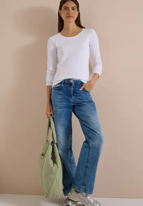 Basic shirt met lange mouwen en ronde hals White Frau trägt weißes Langarmshirt, blaue Jeans und hält eine gesteppte grüne Tasche.