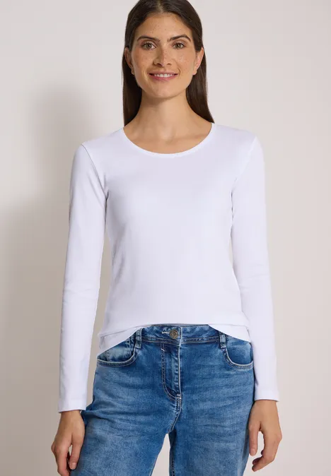 Basic shirt met lange mouwen en ronde hals White Eine Frau in weißem Langarmshirt und Jeans vor hellem Hintergrund.