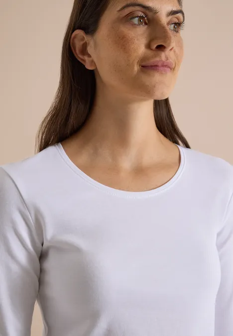Basic shirt met lange mouwen en ronde hals White Junge Frau mit braunen Haaren, im weißen Langarmshirt vor neutralem Hintergrund, seitlich blickend.