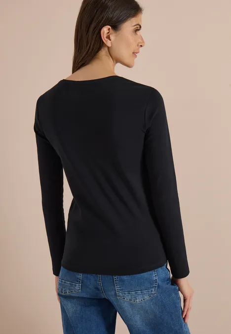 Basic shirt met lange mouwen en ronde hals Black Frau von hinten in schwarzem Langarmshirt und blauen Jeans vor beigem Hintergrund.