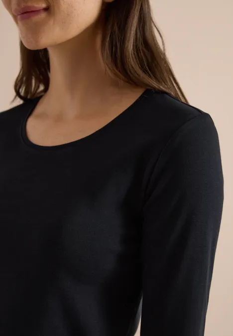 Basic shirt met lange mouwen en ronde hals Black Eine Frau trägt ein schlichtes schwarzes Langarmshirt mit rundem Ausschnitt.