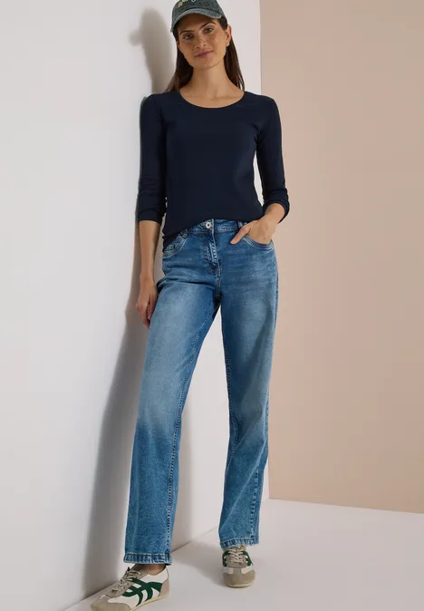 Basic Langarm Shirt mit Rundhals universal blue Eine Frau lehnt entspannt an einer Wand und trägt ein dunkelblaues Shirt, Jeans, Baseballcap und Turnschuhe.