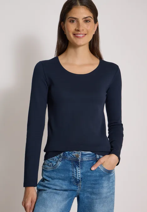 Basic Langarm Shirt mit Rundhals universal blue Eine lächelnde Frau trägt eine dunkelblaue Langarmbluse und eine blaue Jeans vor neutralem Hintergrund.