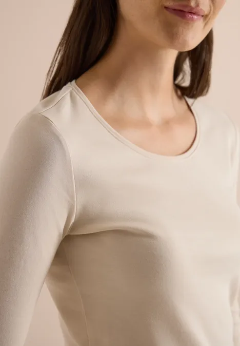 Basic shirt met lange mouwen en ronde hals pearl beige Nahaufnahme einer Frau in cremefarbenem, eng anliegendem Langarmshirt vor neutralem Hintergrund.