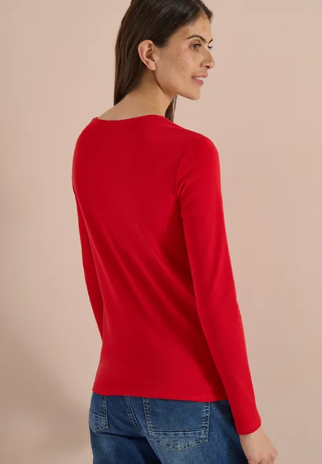Basic shirt met lange mouwen en ronde hals flame red Frau von hinten in rotem Langarmshirt und blauen Jeans vor beigem Hintergrund.