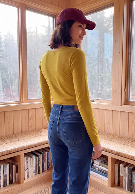 T-shirt basique à manches longues et col rond golden honey Eine Frau in roter Cap, gelbem Langarmshirt und Jeans blickt über die Schulter in einem hellen Holzraum.