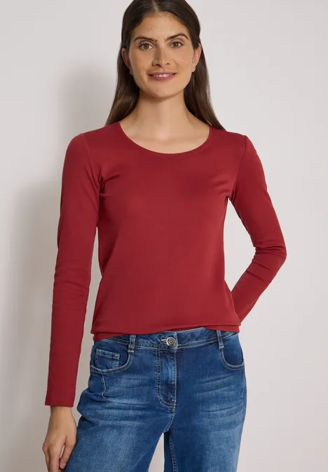 Basic Langarm Shirt mit Rundhals russet red Frau mit langärmligem rotem Shirt und blauen Jeans steht vor hellem Hintergrund.