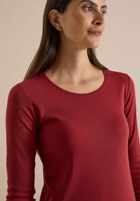 Basic Langarm Shirt mit Rundhals russet red Nahaufnahme einer Frau in rotem, langärmeligem Shirt vor neutralem Hintergrund.