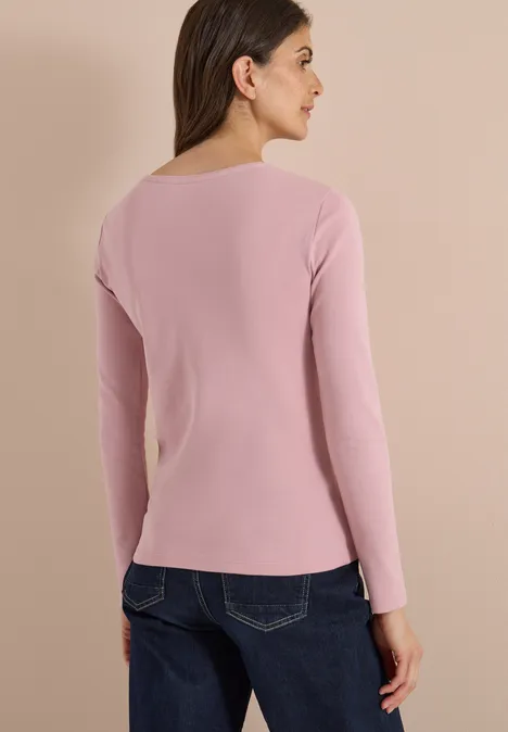 Femme de dos portant un t-shirt à manches longues rose et un jean bleu sur fond clair