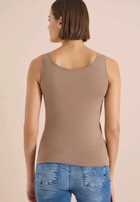 Femme de dos portant un débardeur marron et un jean, sur fond neutre.