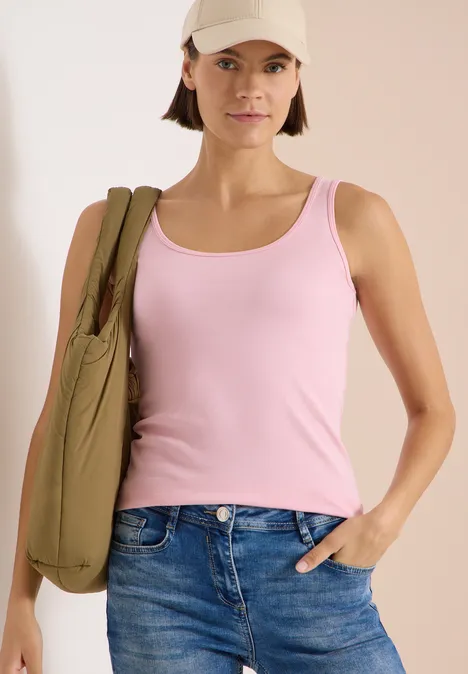 Frau in rosa Tanktop und Jeans trägt eine grüne Umhängetasche, Hand in der Hosentasche.