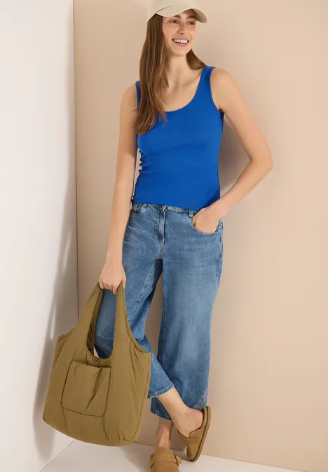 Eine Frau trägt ein blaues Tanktop, weite Jeans und hält eine olivgrüne Handtasche.