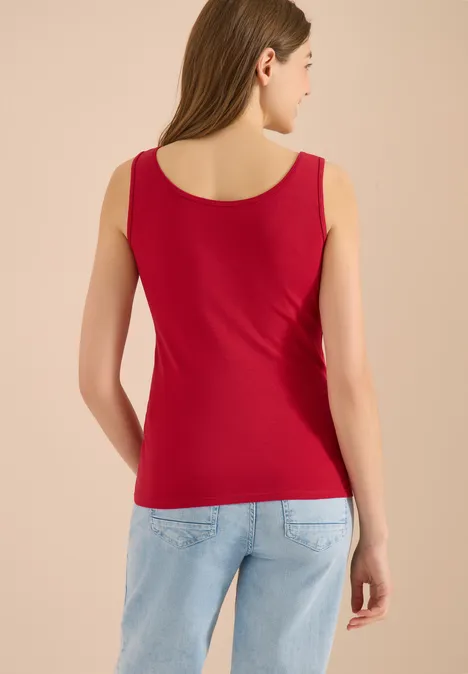 Rückenansicht einer Frau in rotem Tanktop und hellblauen Jeans.
