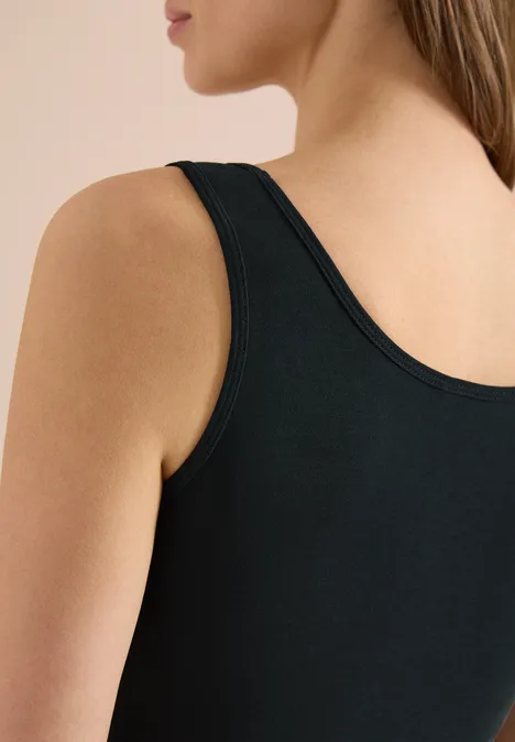 Close-up van een vrouw in een zwarte mouwloze top, met focus op schouder en rug.