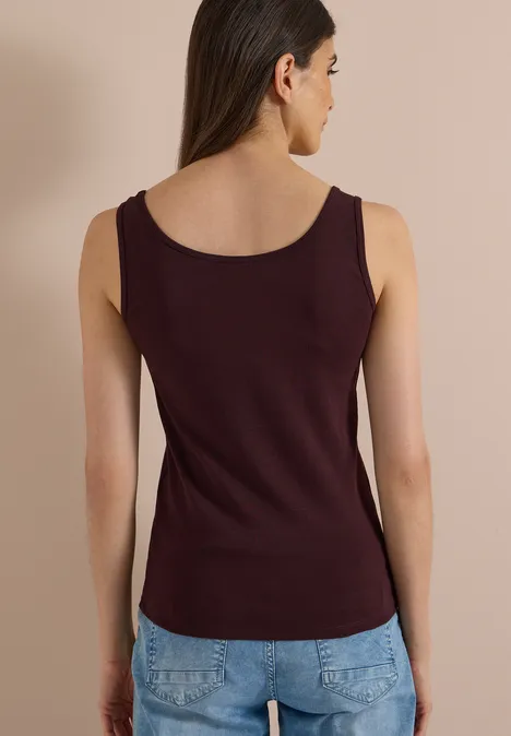 Basic top van puur katoen berry red Eine Frau von hinten in ärmellosem, weinrotem Top und blauen Jeans.