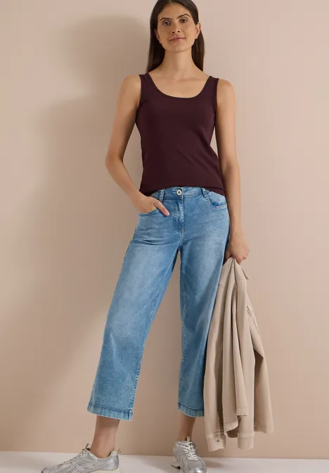 Basic top van puur katoen berry red Modell trägt weite Jeans, bordeauxfarbenes Top und hält eine beige Jacke.