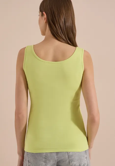 Vue arrière d’une femme en top vert citron et jeans gris.