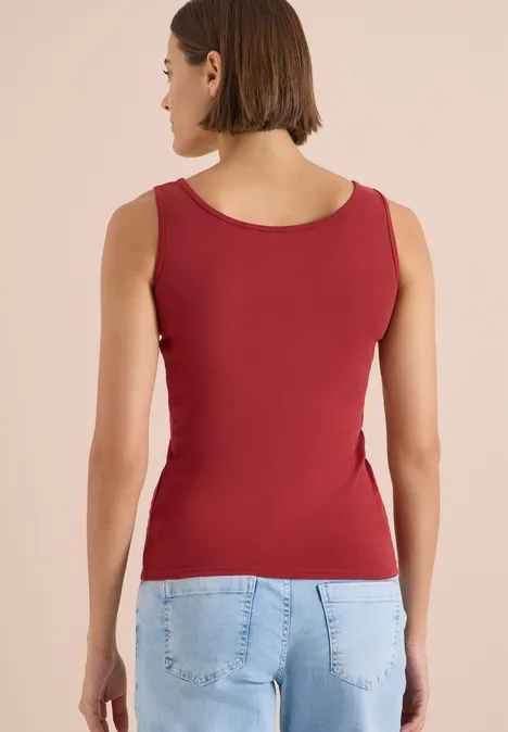 Frau von hinten in rotem Top und blauen Jeans vor neutralem Hintergrund.