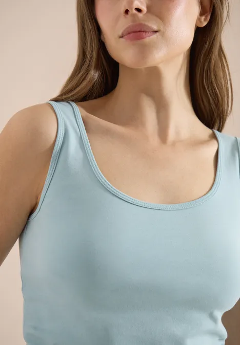 Femme en débardeur bleu clair, gros plan sur les épaules et le buste.