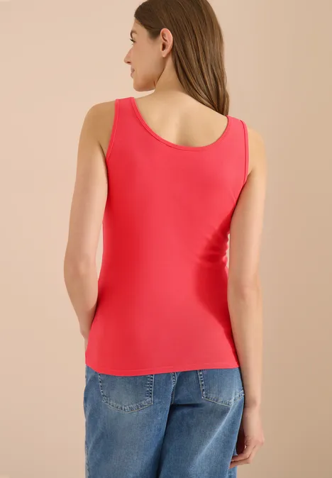 Frau von hinten in rotem Tanktop und blauer Jeanshose vor hellem Hintergrund.