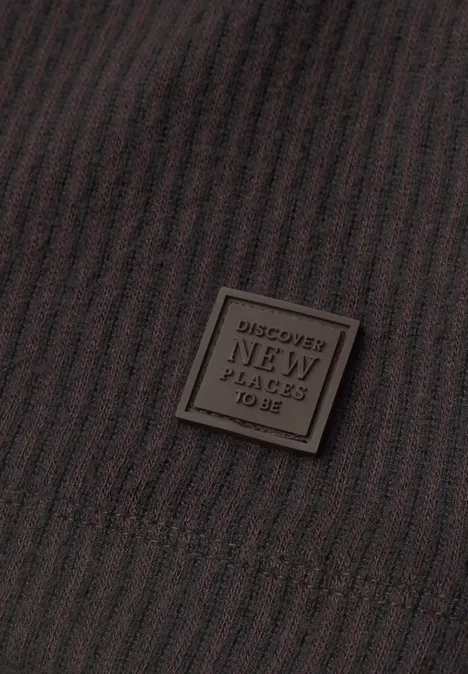 Braune gerippte Textur mit einem quadratischen Lederpatch 'DISCOVER NEW PLACES TO BE'.