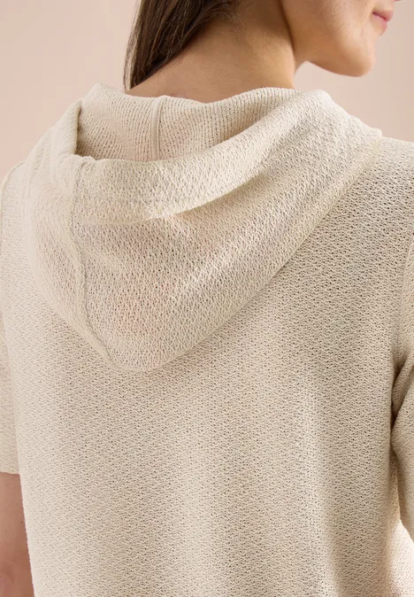 Rückansicht einer Frau in einem beige strukturierten Kurzarm-Kapuzenpullover.
