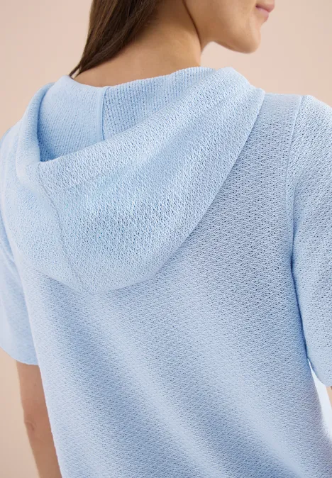 Person von hinten mit hellblauem, strukturiertem Kapuzenpullover.