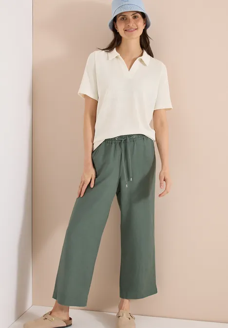 Effen polo met korte mouwen macadamia beige Vrouw in crème poloshirt en wijde groene stoffen broek voor effen achtergrond