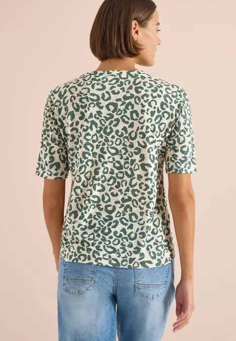 Femme vue de dos portant un t-shirt vert à motif léopard et un jean bleu clair.