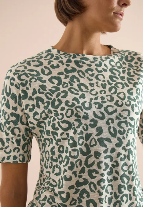 Femme portant un pull à manches courtes crème à motifs léopard verts.
