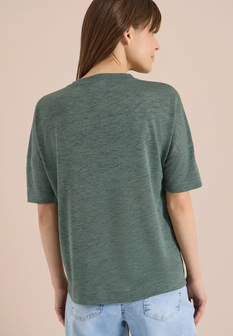 Person steht mit dem Rücken zur Kamera, trägt grünes T-Shirt und Jeans.