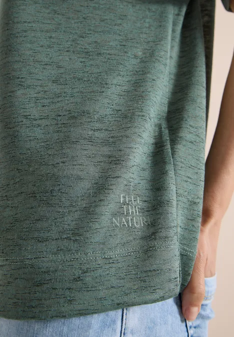 Teilansicht einer Person in grün meliertem T-Shirt mit 'FEEL THE NATURE'-Aufdruck und Jeans.